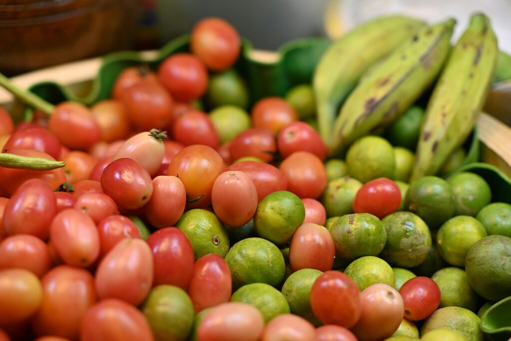 DFC 5257- Fresh tropical bounty, ripe cherry tomatoes, green limes and bananas piled together at a local Thai market.